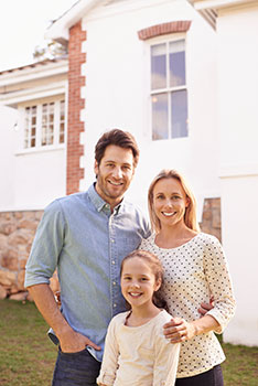 Parents and daughter standing in front of their new home, smiling